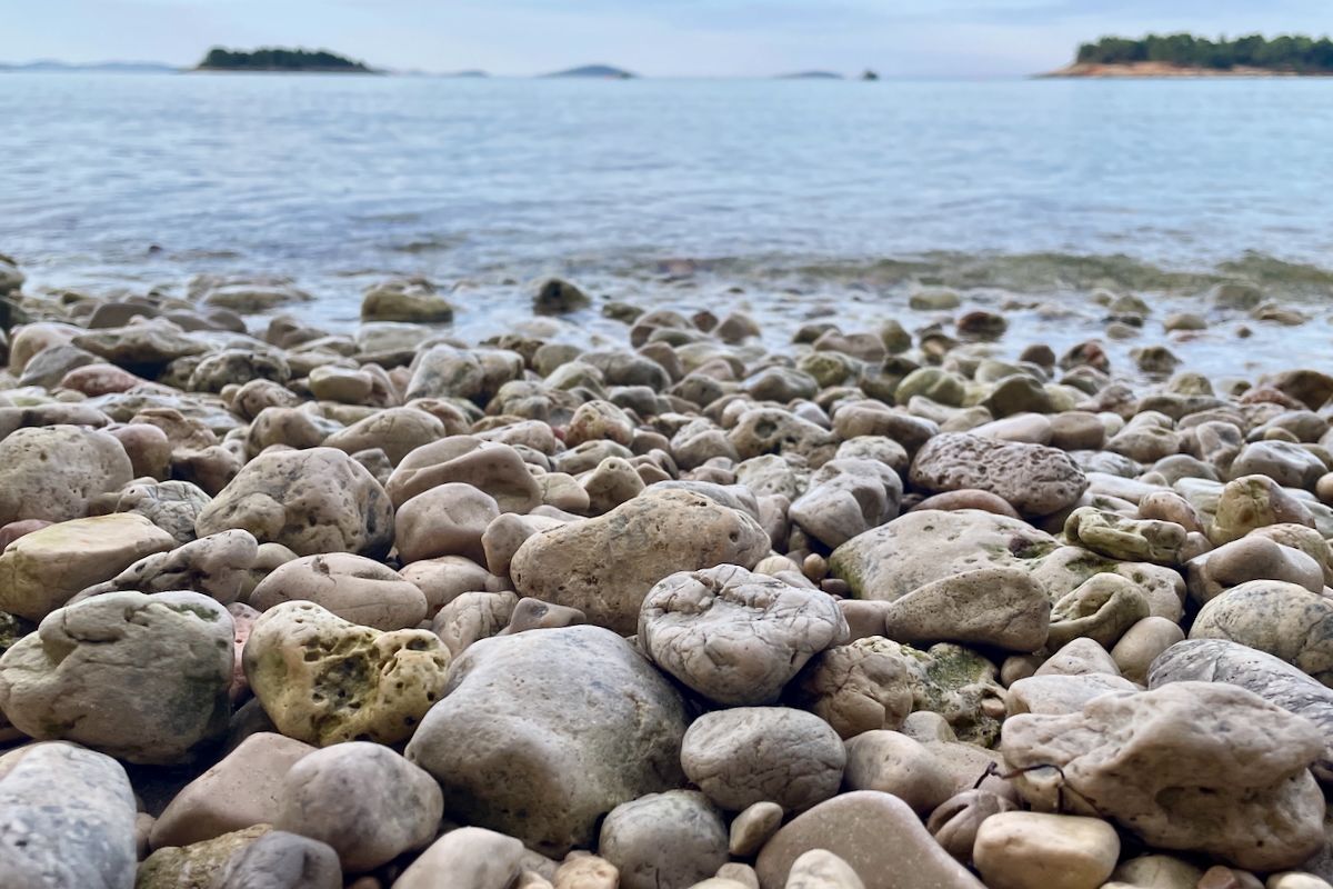 Kiezelstrand Een stapel stenen op een strand met een watermassa op de achtergrond.