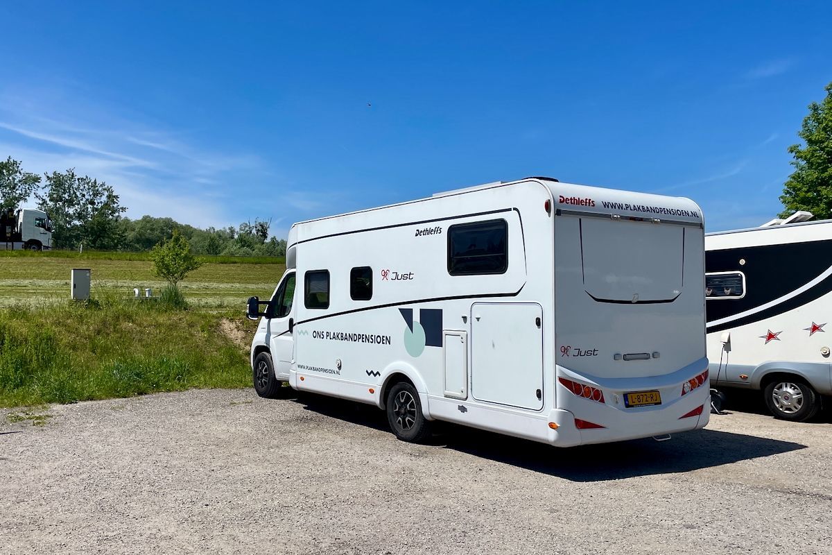 Onze overnachtingsplek Een witte camper staat geparkeerd op een grindterrein.