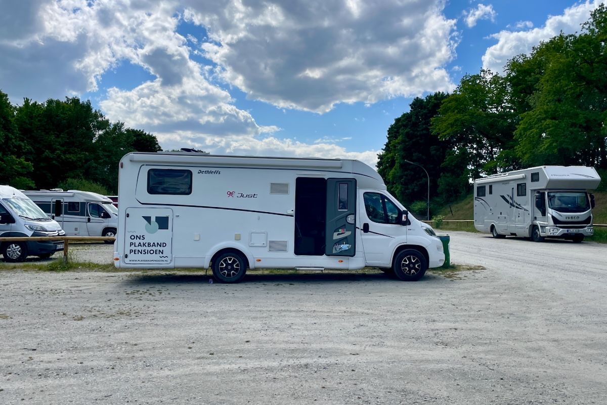 Onder een wat donker wolkendek Een witte camper staat geparkeerd op een parkeerplaats.