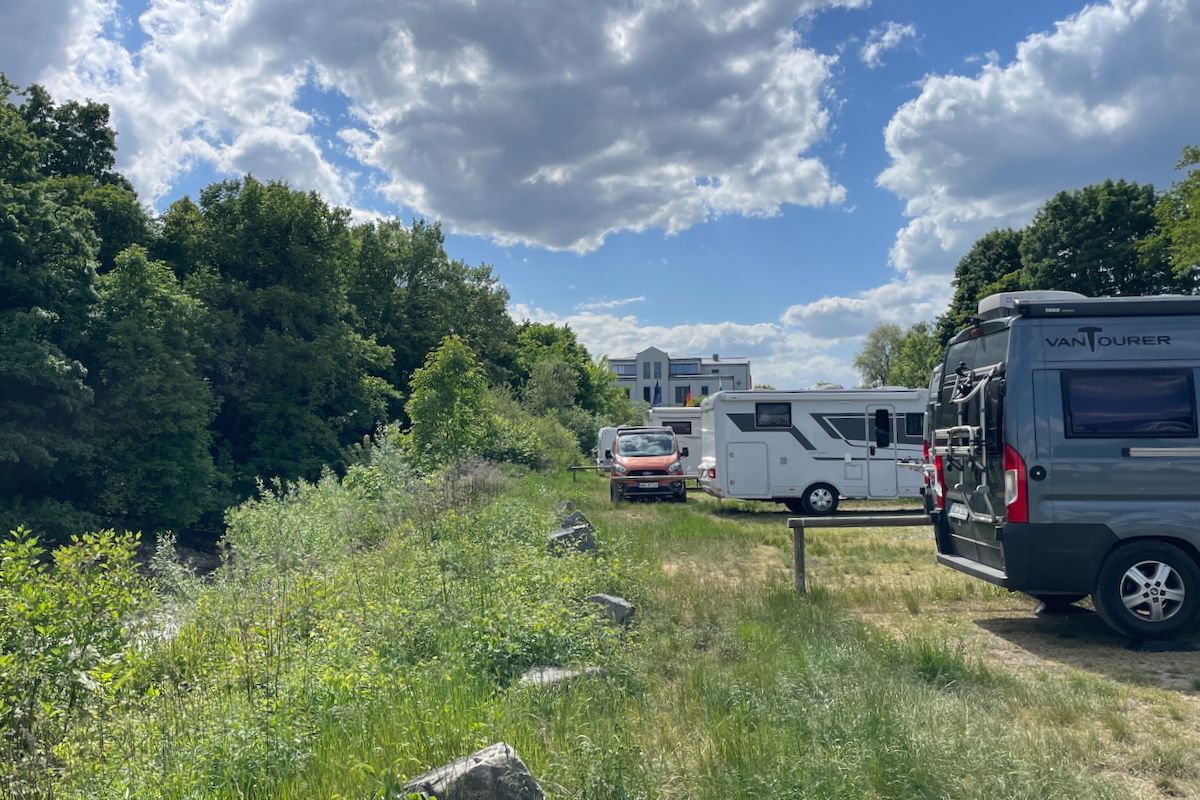 Drukte aan de Donau Een groep campers staat geparkeerd in een veld naast een rivier.