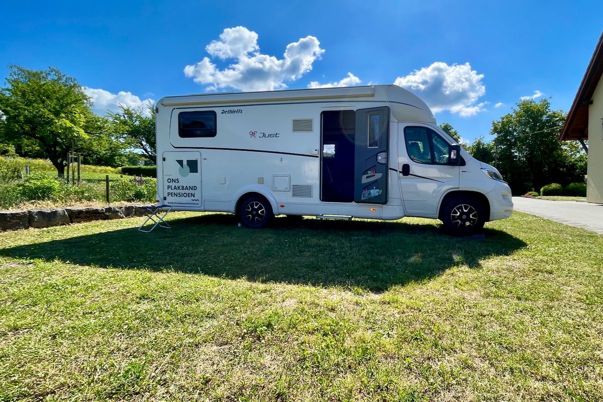Bijna klaar voor vertrek Een witte camper staat geparkeerd in een grasveld voor een huis.