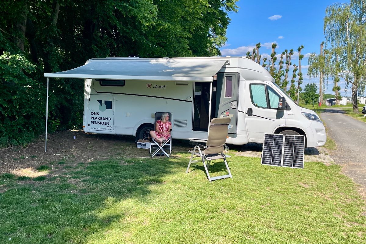 Het slaapplaatsje Een witte camper staat geparkeerd in een grasveld met een luifel en stoelen.