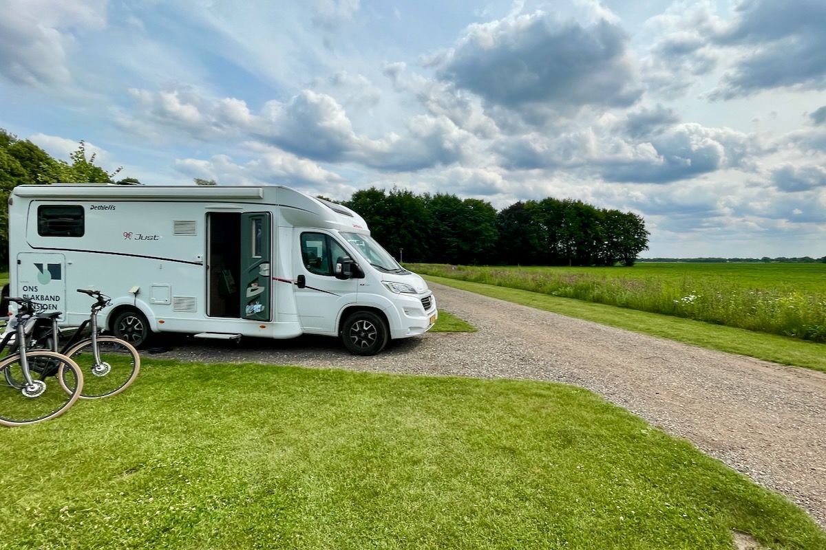 Onze plek op Cp Loosterstee Een witte camper staat geparkeerd langs een onverharde weg.