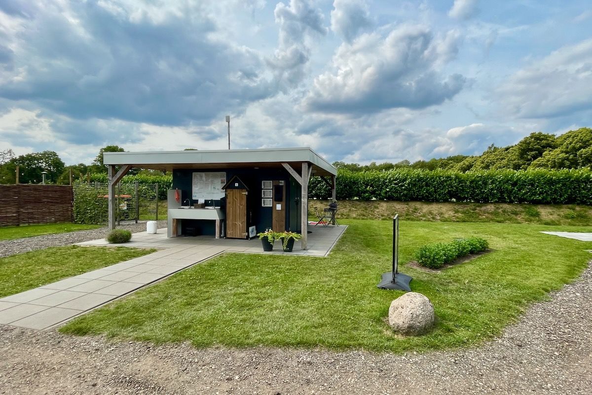 Het sanitair gebouw Een klein huisje staat midden in een grasveld.