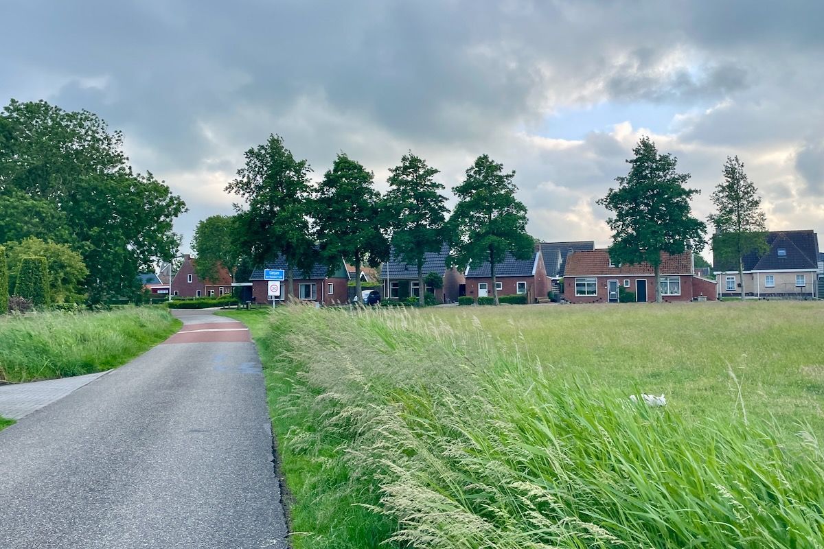 Eanjum of Anjum Een weg die door een grasveld gaat met huizen op de achtergrond.