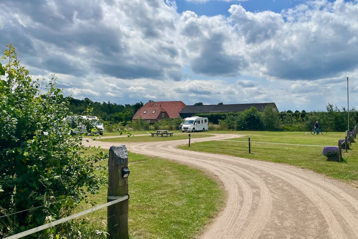 Het 2e veld Een onverharde weg door een grasveld met een huis op de achtergrond.
