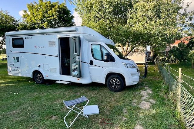 Een witte camper staat geparkeerd in een grasveld naast een hek.