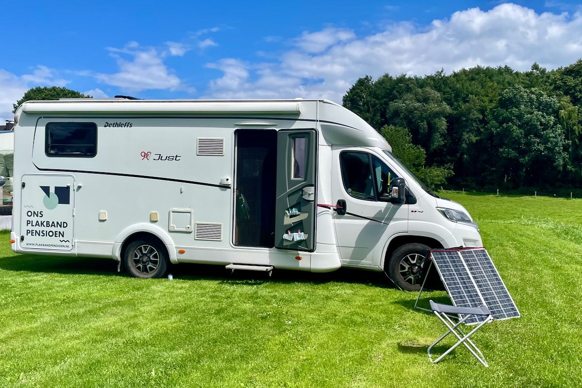 Onze plek bij Hof an der Hese Witte camper geparkeerd op een grasveld met een open deur. Er staan draagbare zonnepanelen in de buurt.