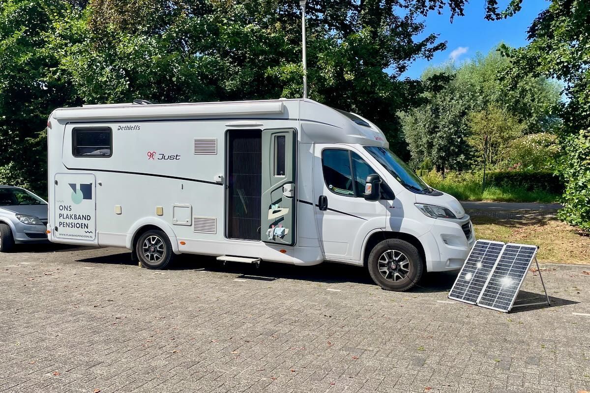 Genoeg 'power' Witte camper geparkeerd op grind met open deur en zonnepaneel.