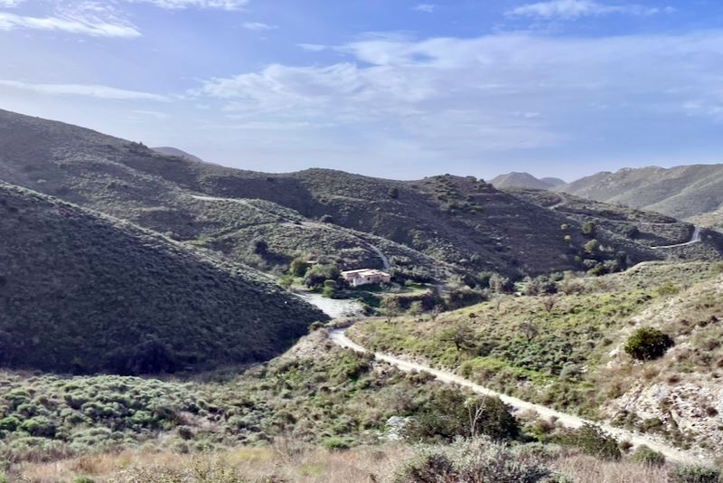 Glooiende heuvels met een onverharde weg die naar een klein gebouw leidt, onder een stralende hemel.