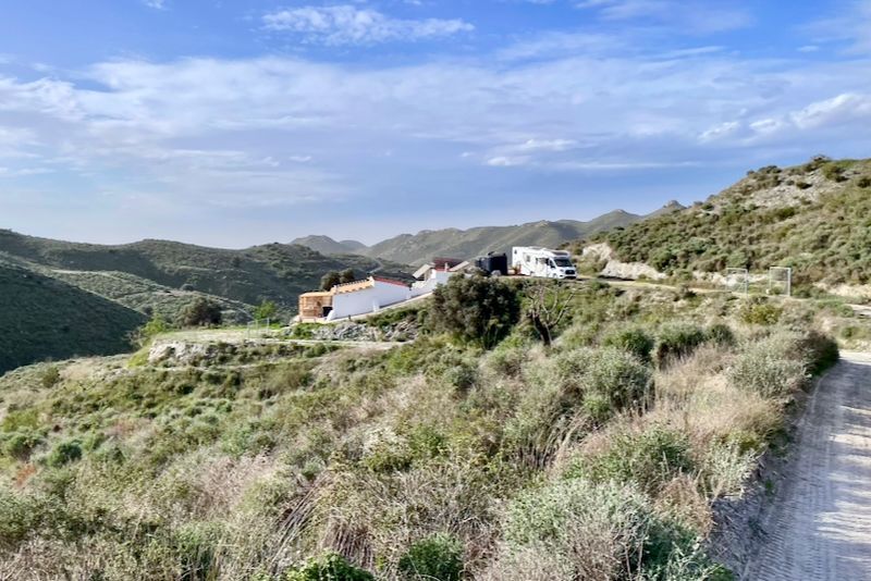 Glooiende, groene heuvels met witte gebouwen en een camper onder een gedeeltelijk bewolkte blauwe lucht.