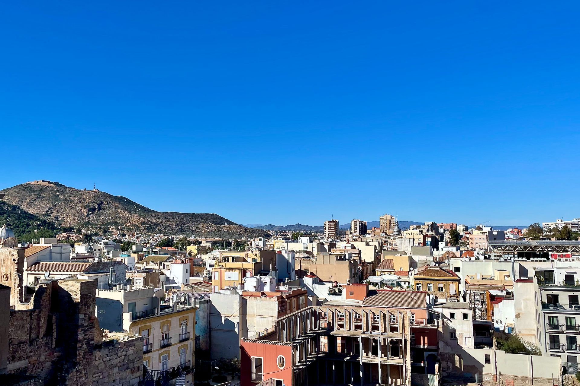 Stadsgezicht met gebouwen onder een blauwe lucht, bergen op de achtergrond.
