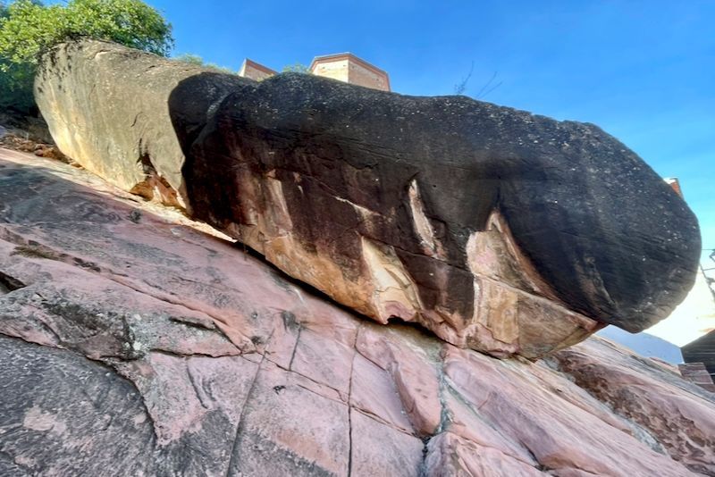 Groot, donkerkleurig rotsblok op een roodroze rotshelling, met een helderblauwe lucht.