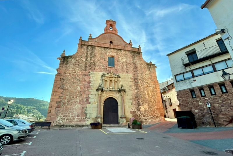 Een kerkgebouw van baksteen op een plein met auto's die ernaast geparkeerd staan. Blauwe lucht.