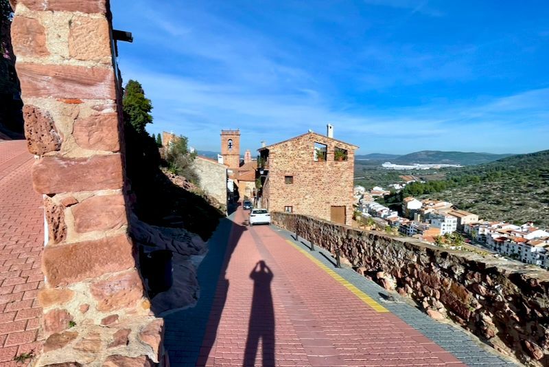Een bakstenen weg voert door een historisch dorp met stenen gebouwen onder een zonnige hemel.