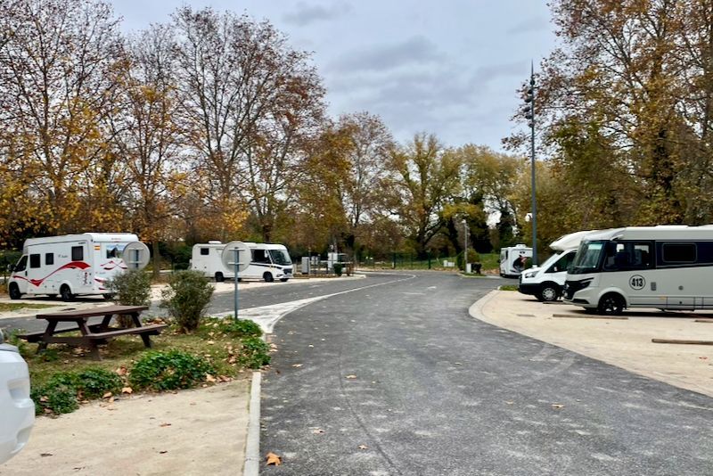 Campers geparkeerd op een verhard terrein; picknicktafel links, bomen op de achtergrond, bewolkte lucht.