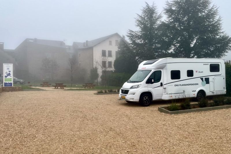 Witte camper geparkeerd op grind, met een gebouw op de achtergrond op een mistige dag.