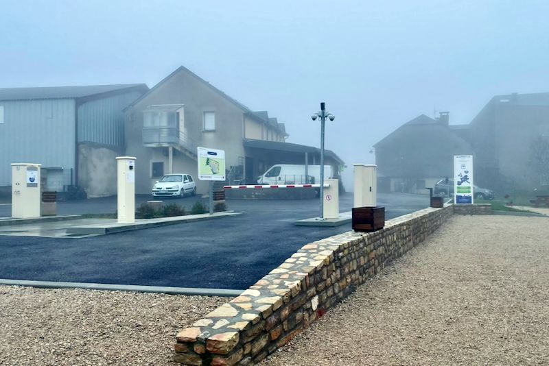 Ingang van een gebouw op een mistige dag, met een slagboom, een stenen muur en verschillende gebouwen op de achtergrond.
