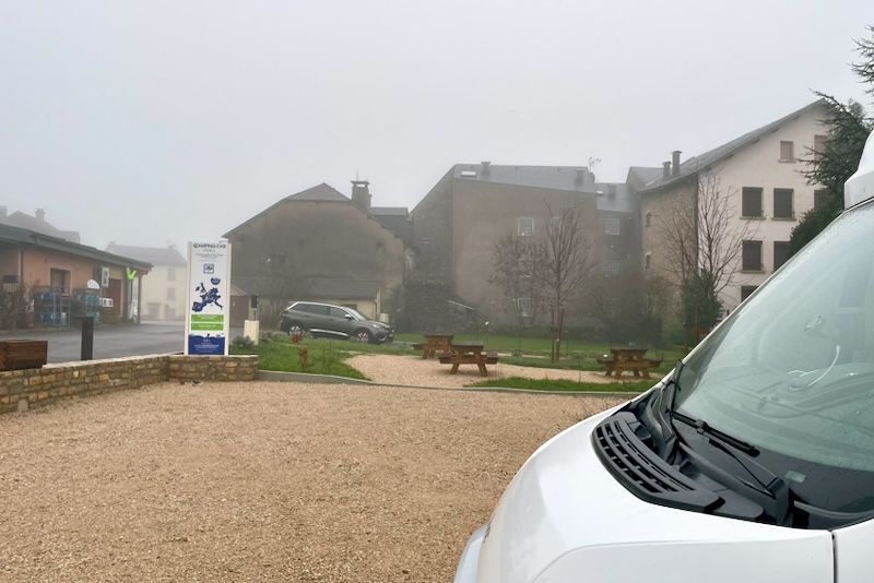 Uitzicht op een klein stadsplein op een mistige dag, met een wit voertuig op de voorgrond.