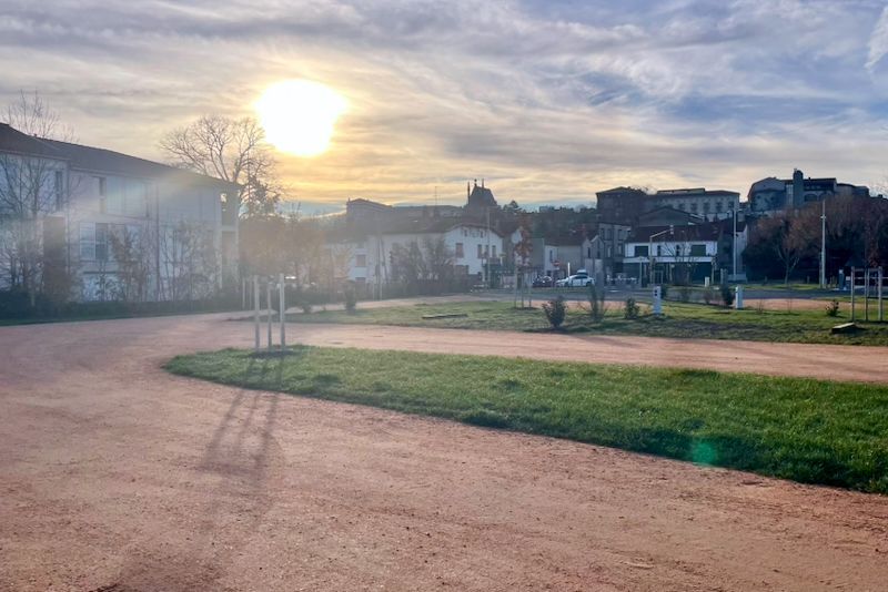 Park met een kronkelend pad, gras en gebouwen in een felle zon.