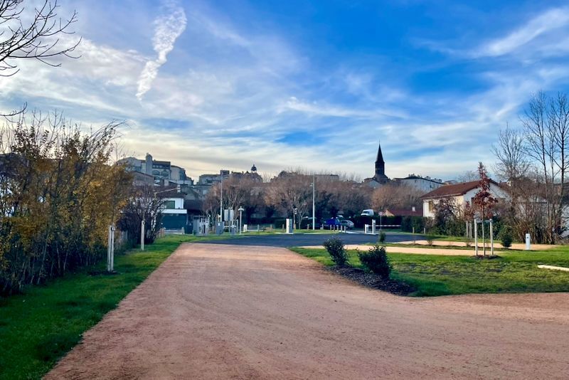 Een grindpad leidt naar een stadje met gebouwen en een kerktoren onder een blauwe lucht.