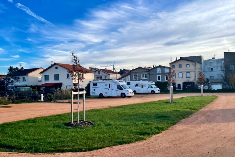 Drie witte campers geparkeerd op grind, vlakbij gras en huizen onder een blauwe lucht.