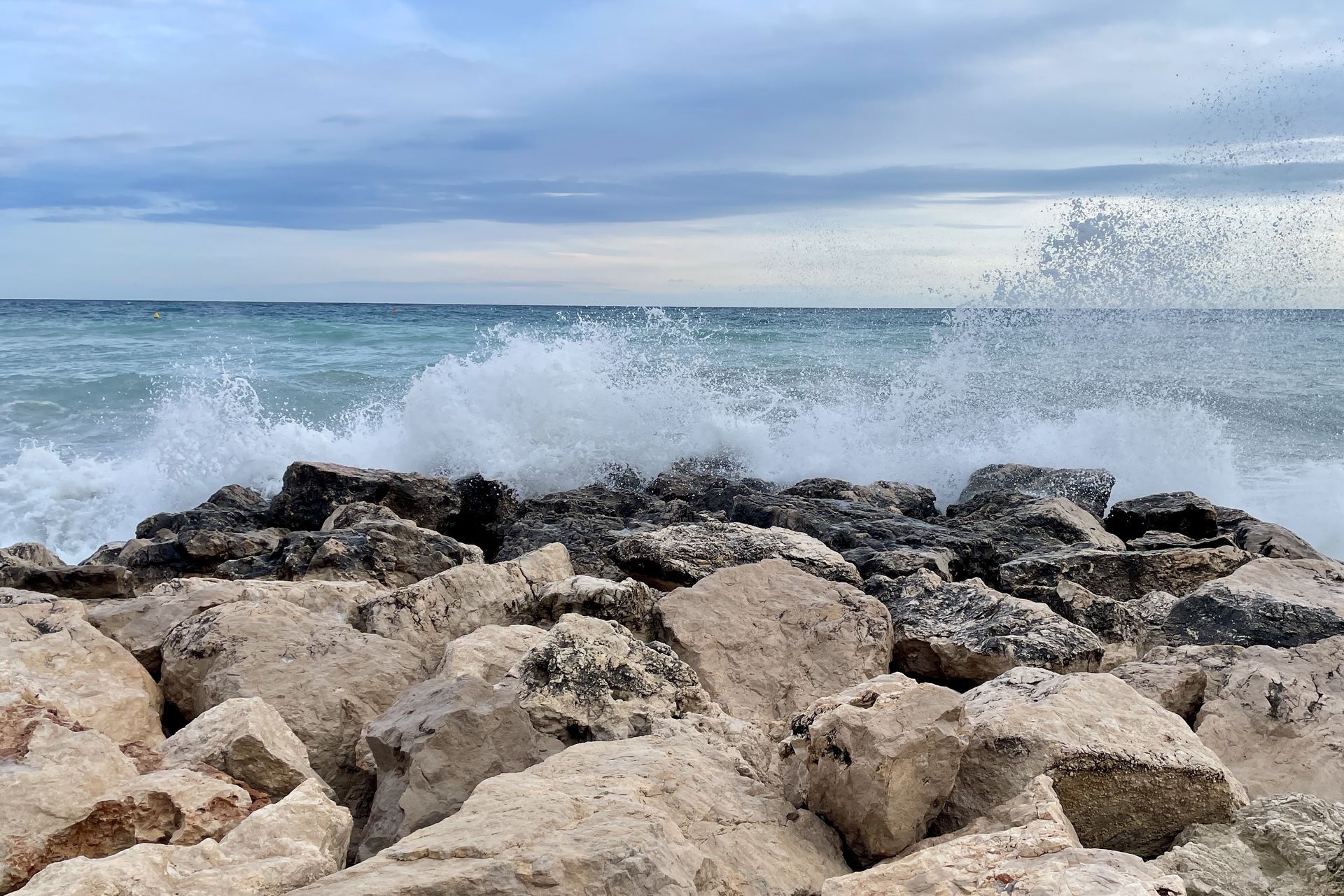 Onstuimig! Golven beuken tegen een stenen golfbreker onder een bewolkte hemel.