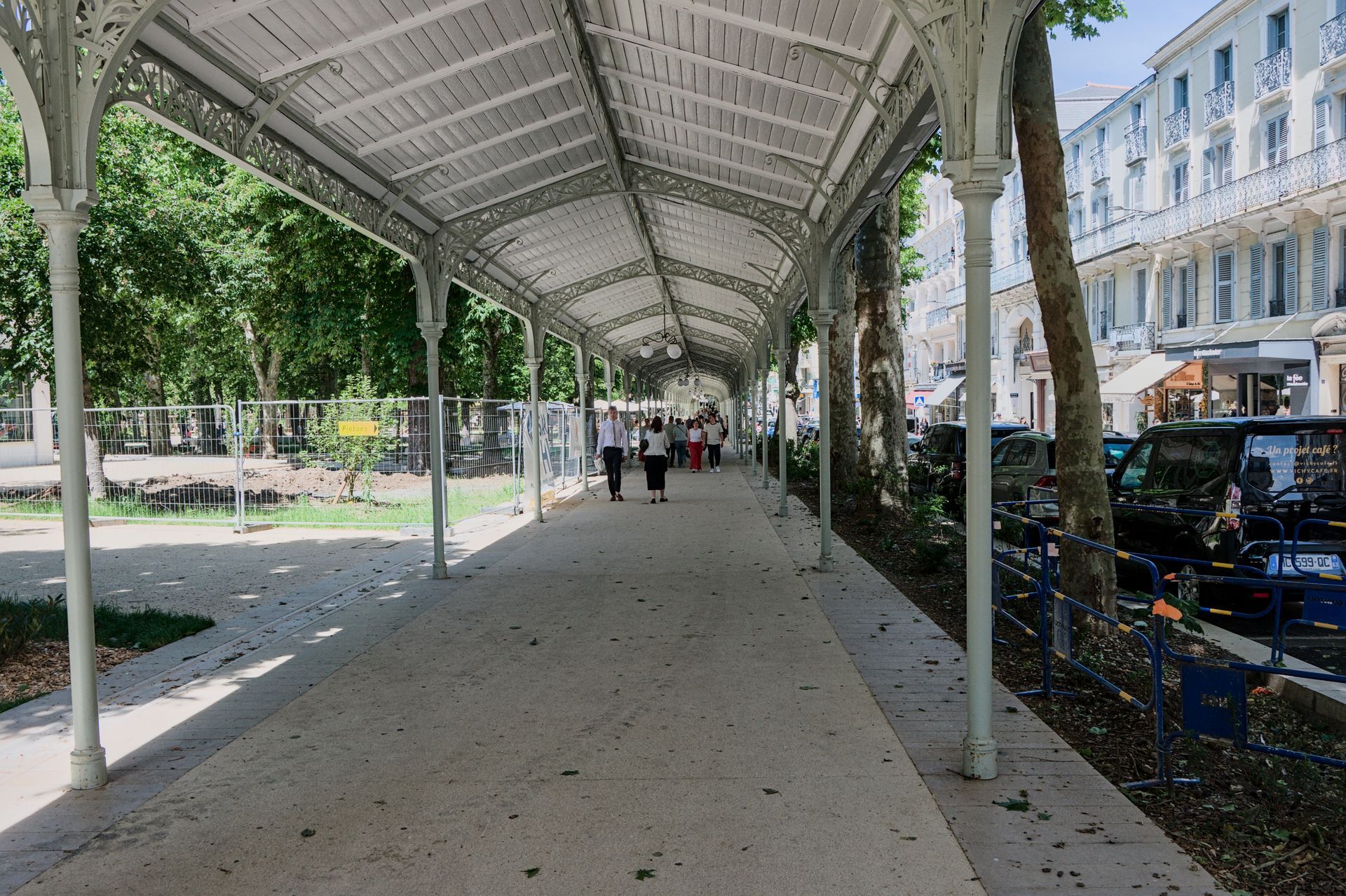 Een overdekte wandelpromenade in een park naast een gebouw, met mensen die in de verte lopen.