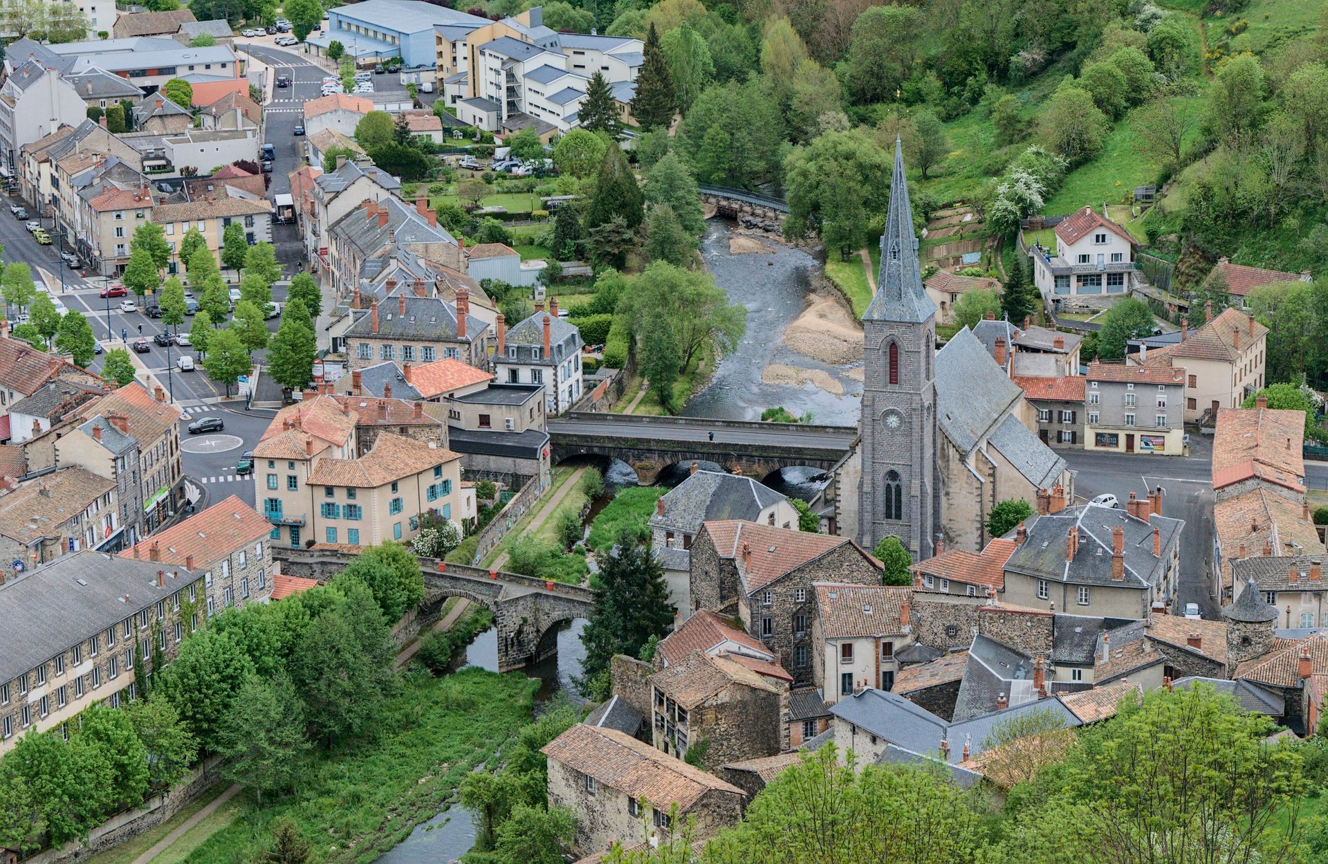 Luchtfoto van een schilderachtig Frans dorp met stenen daken, smalle straatjes en een centrale kerktoren, omgeven door groen.
