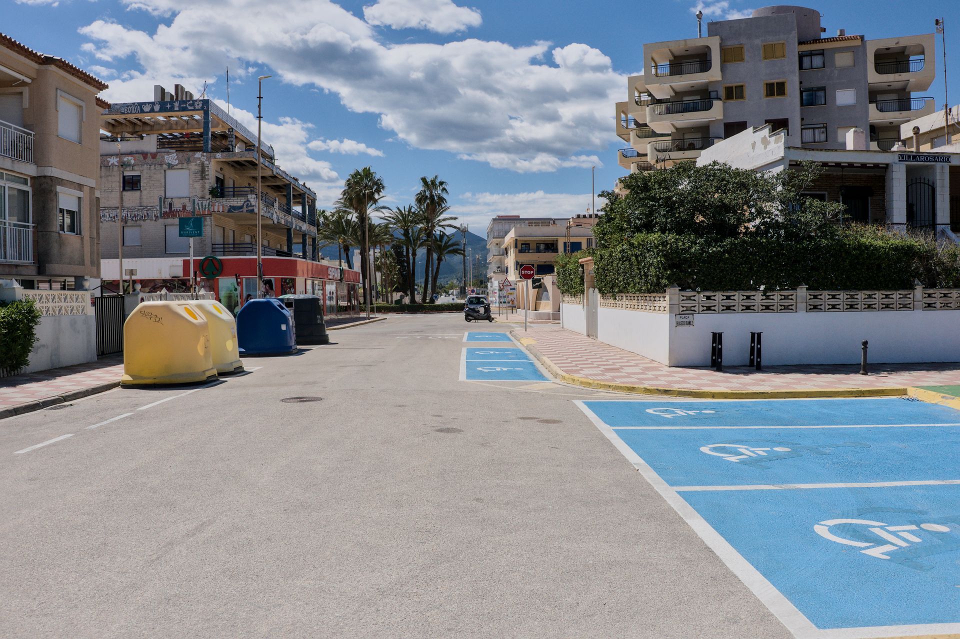 Rustige straat aan zee met blauwe, toegankelijke parkeerplaatsen, appartementen en een bewolkte hemel.