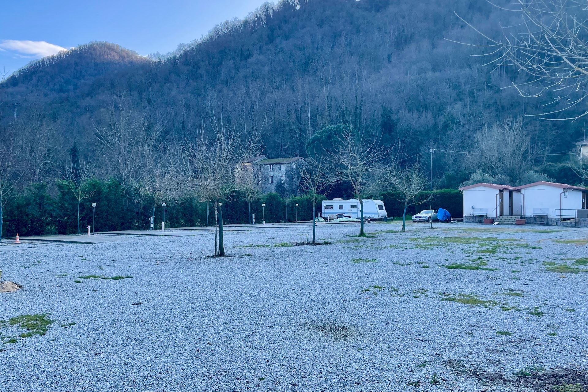 Schaduw in het dal Campingterrein met grindplaatsen, camperplaatsen, kleine gebouwen en een bergachtig landschap.