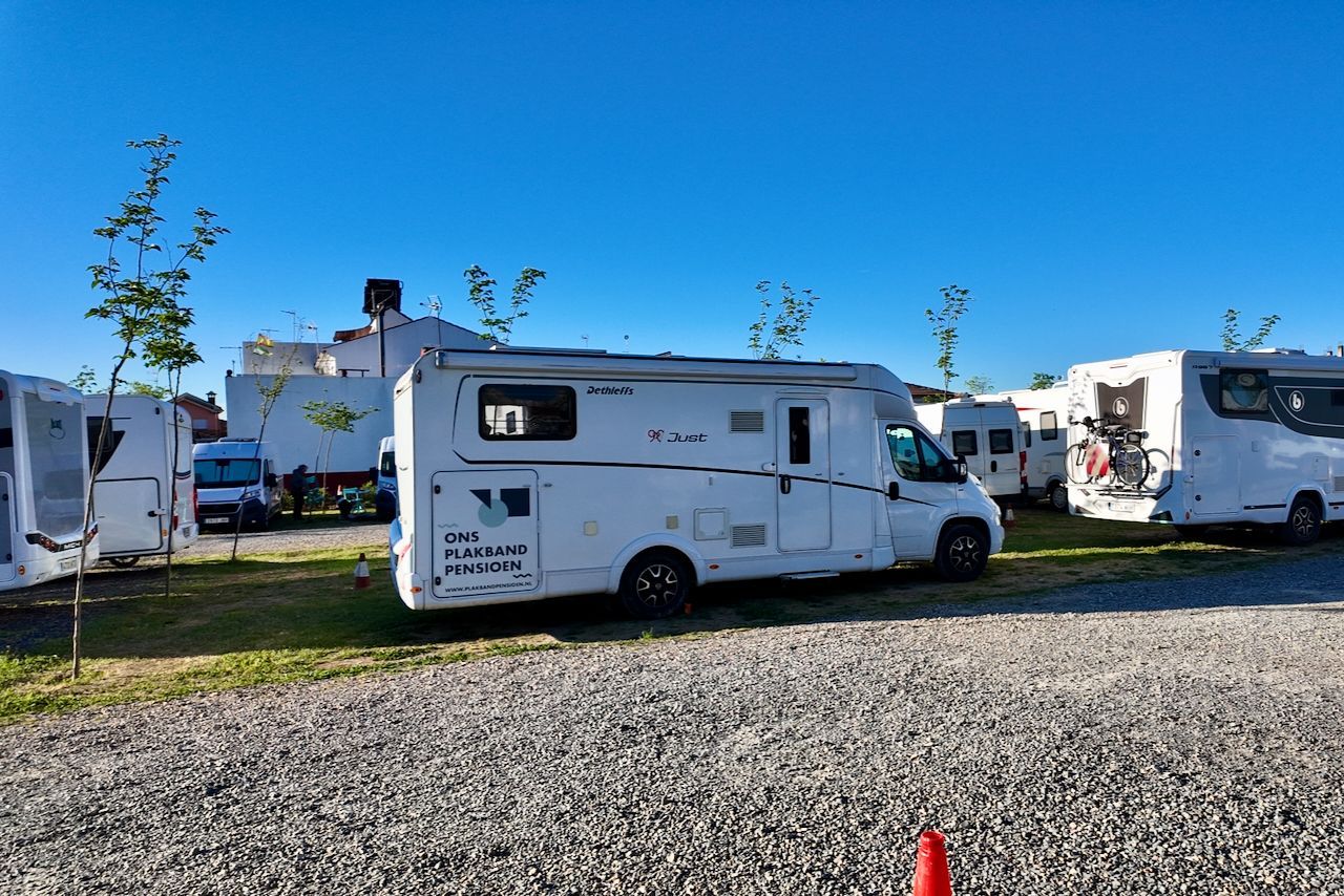 Verschillende witte campers staan ​​geparkeerd op een grindterrein onder een helderblauwe hemel.