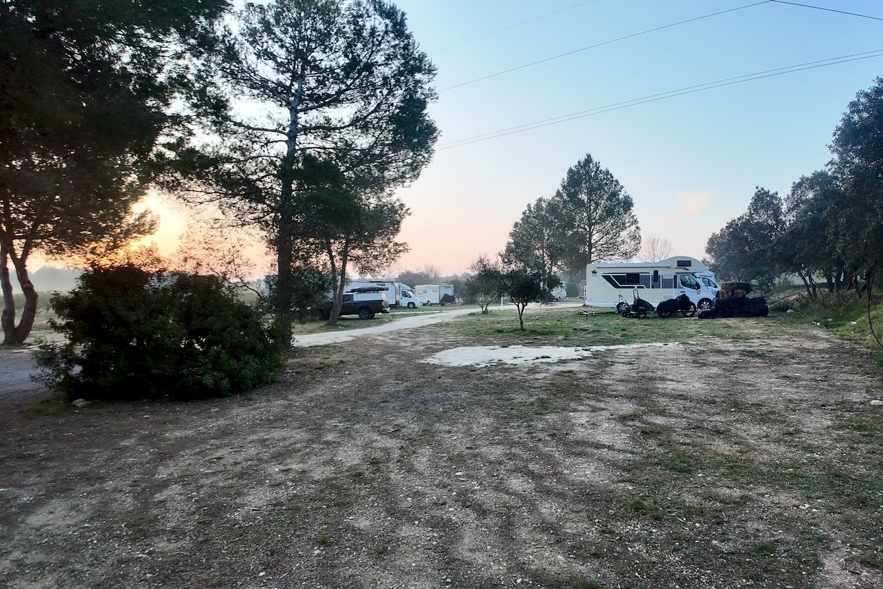 Een camping met campers, bomen en een zandpad bij zonsondergang.