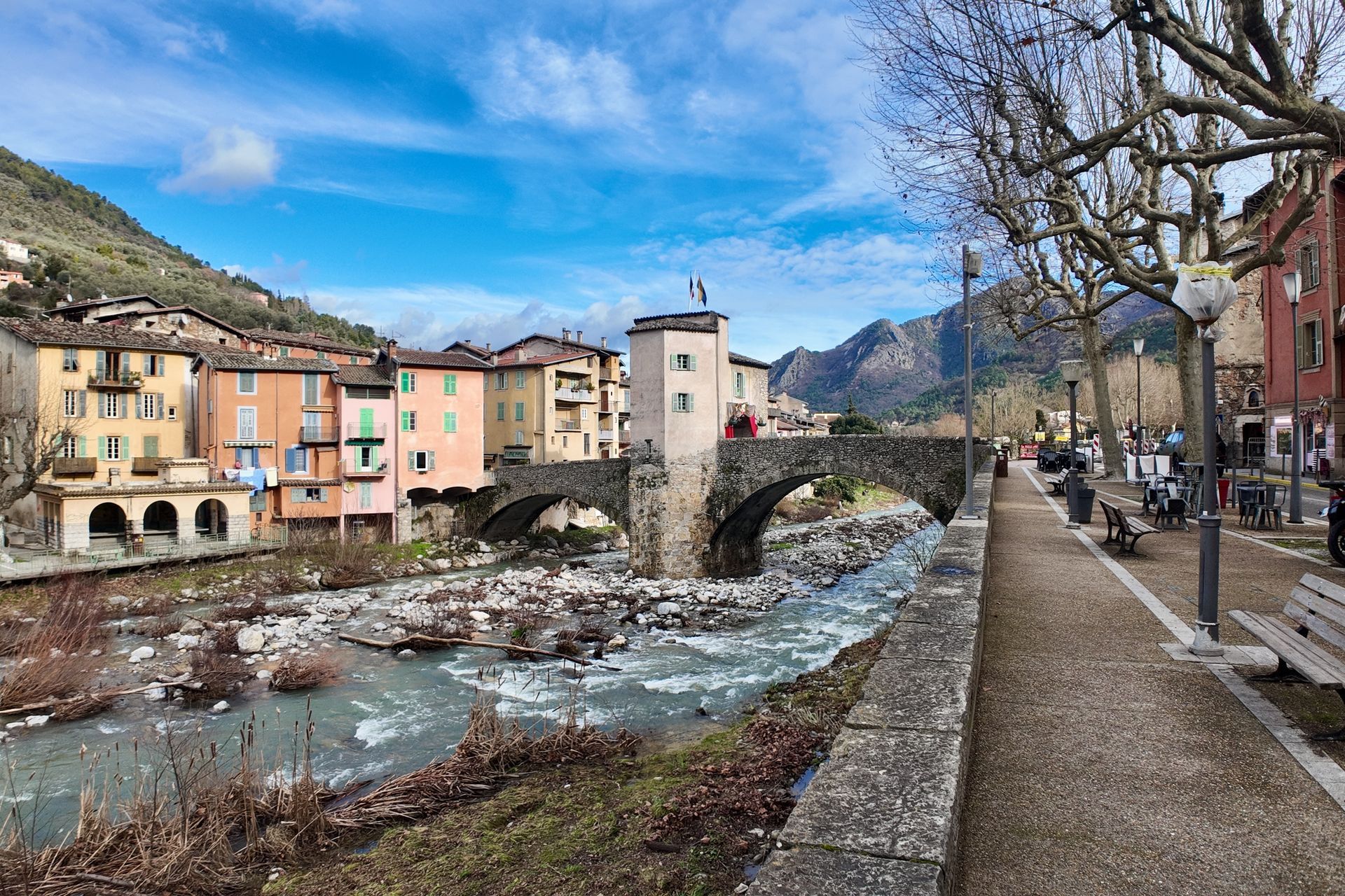Stenen brug over een rivier in een Europees stadje met kleurrijke gebouwen en een wandelpad.