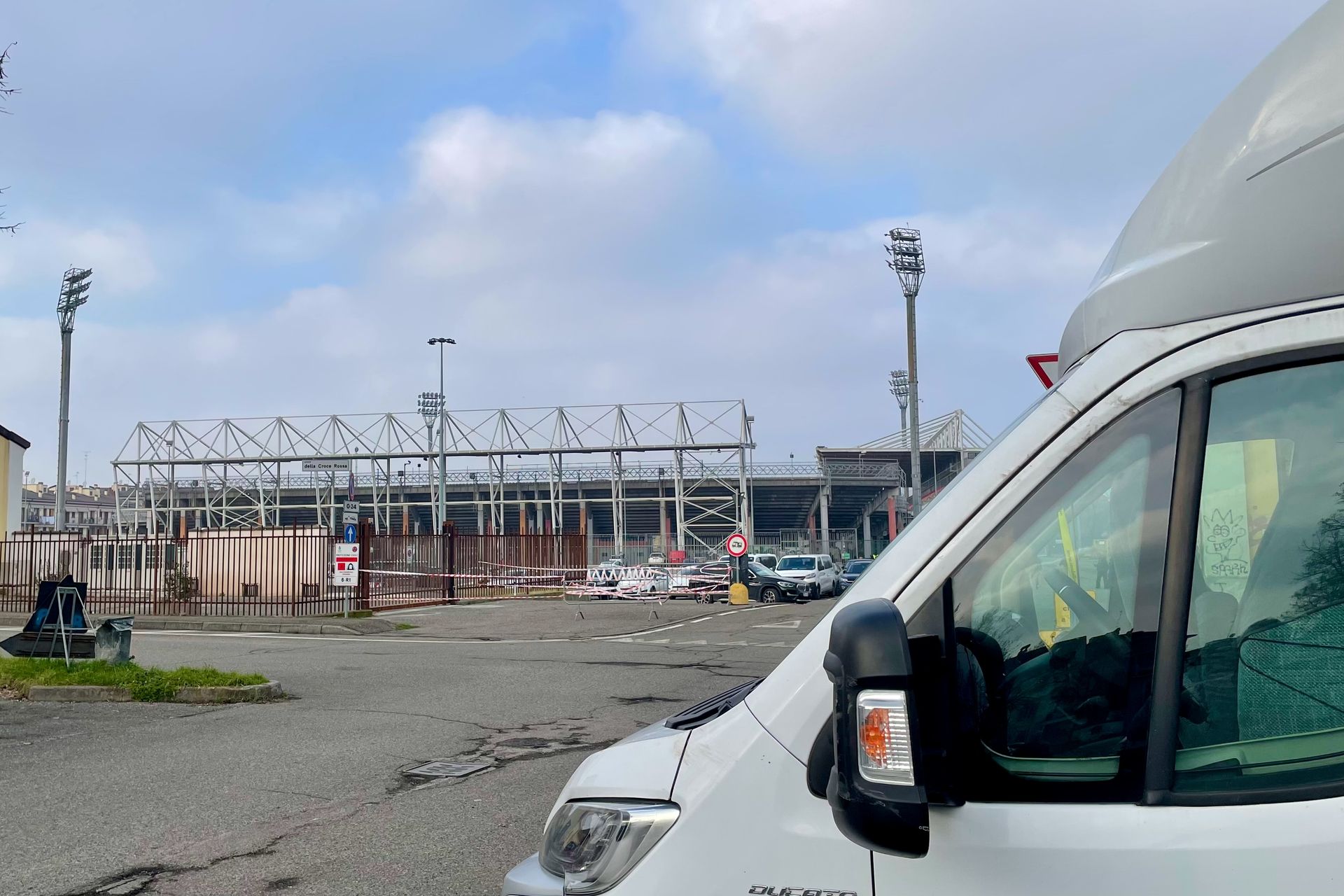 Witte bestelwagen op de voorgrond, industriegebied op de achtergrond met metalen constructies en een bewolkte hemel.