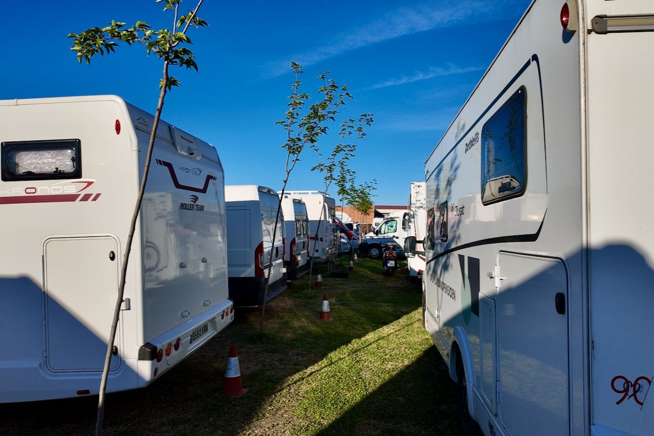 Witte campers staan ​​in rijen geparkeerd op een grasveld onder een helderblauwe hemel.