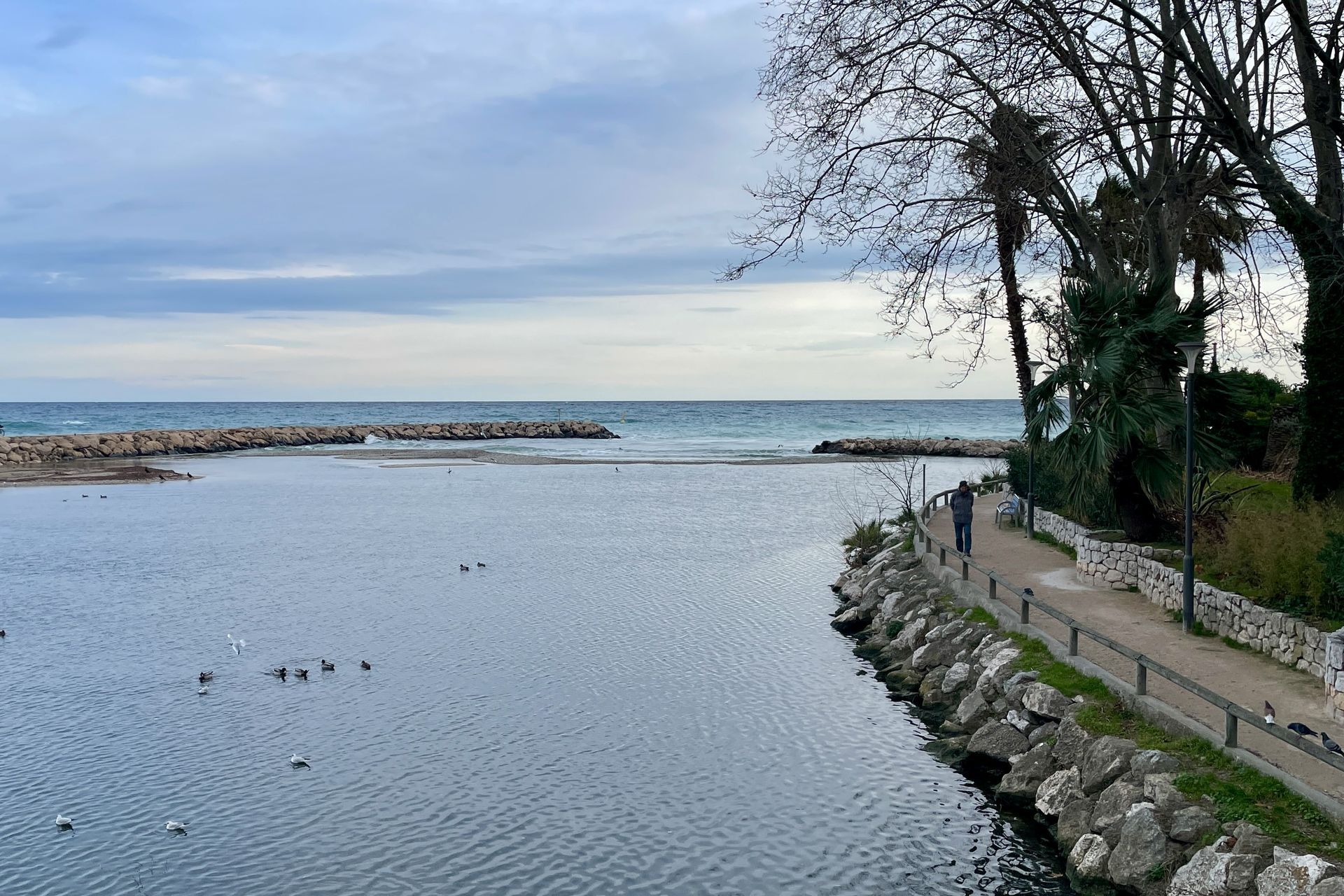Vredig! Rustig water ontmoet de oceaan, een stenen golfbreker, een pad langs de kust, een bewolkte hemel.