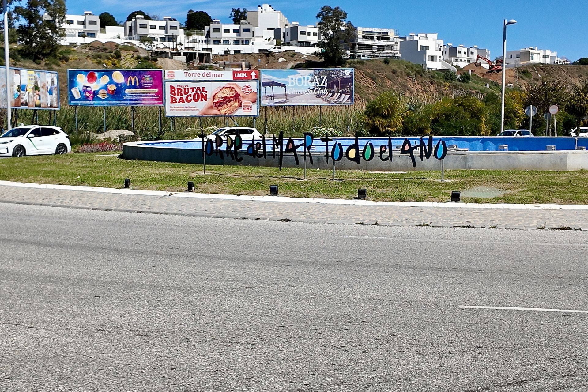 Op een blauwe fonteinmuur in een met gras begroeide rotonde staat in zwarte graffiti de tekst 