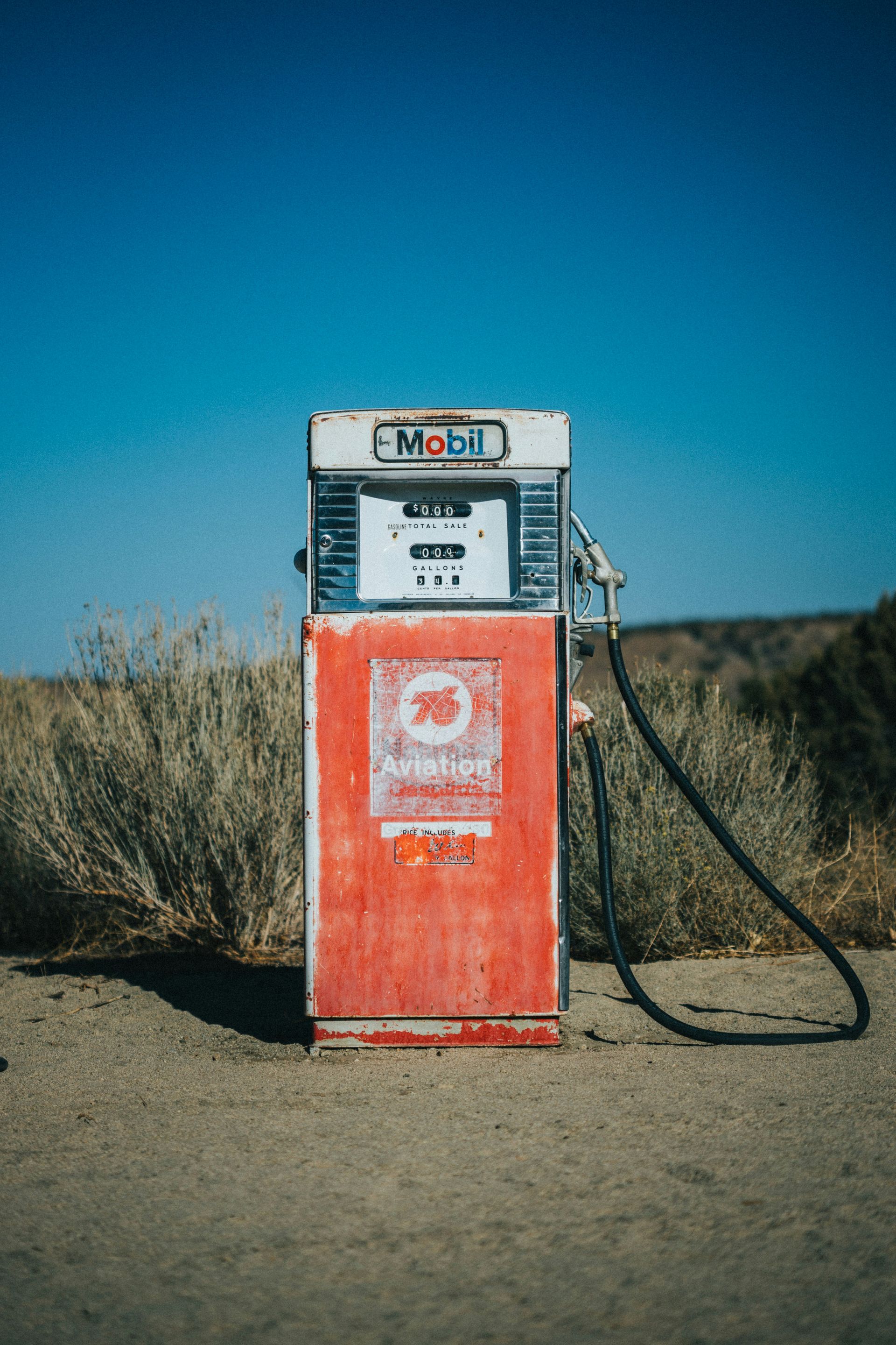 Een rode benzinepomp staat eenzaam in een dor veld onder een helderblauwe hemel.