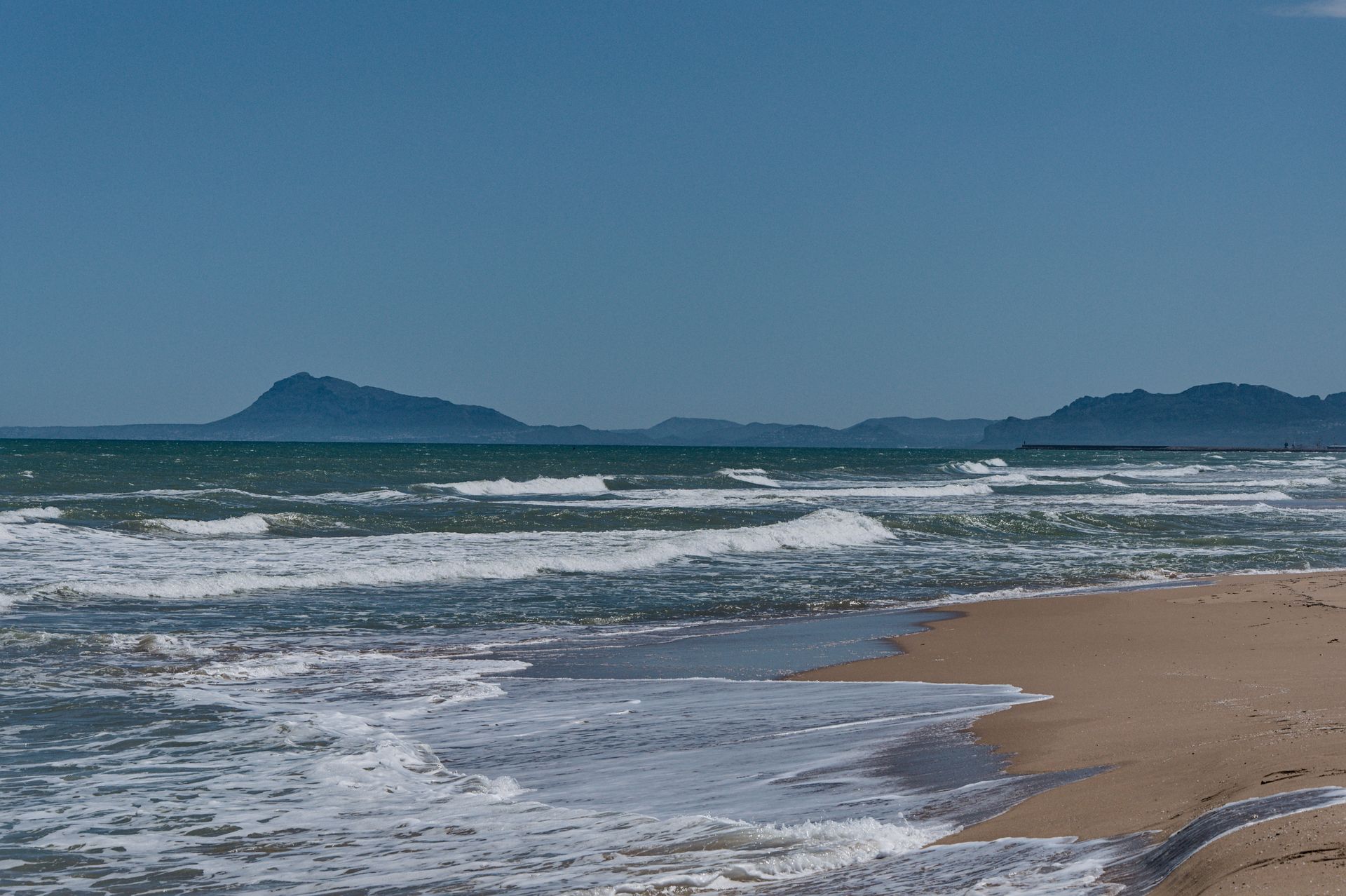 Sandy beach with waves and a distant island under a clear blue sky