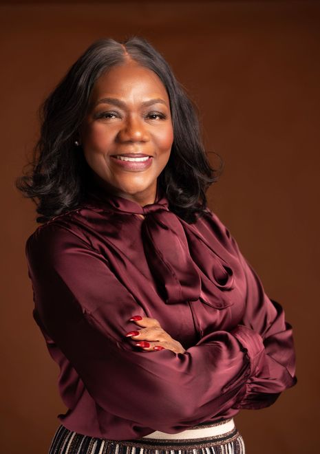 Kedra M. Gotel with folded arms in a burgundy blouse against a warm brown background