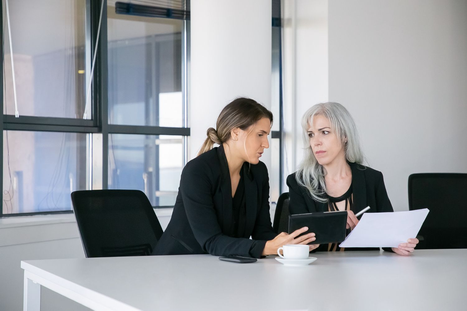 Two colleagues in a meeting, reviewing documents at a white conference table.