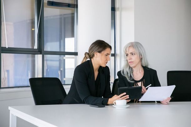 Two colleagues in a meeting, reviewing documents at a white conference table.