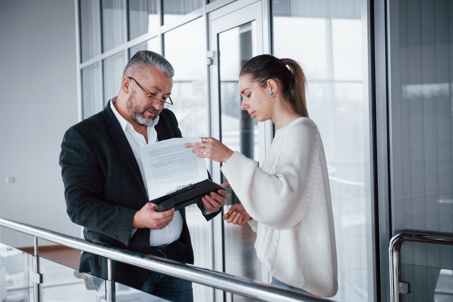 Two coworkers reviewing a document in a bright office hallway