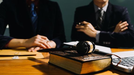 Gavel on a law book in a courtroom, with two businesspeople seated behind it at a table.