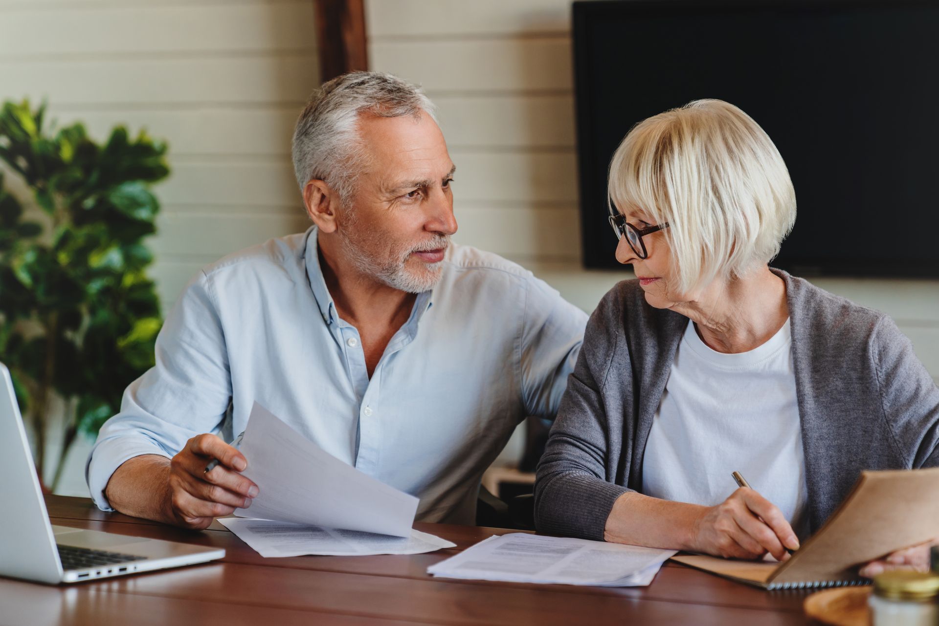 Two people reviewing papers at a table with a laptop in a bright home office
