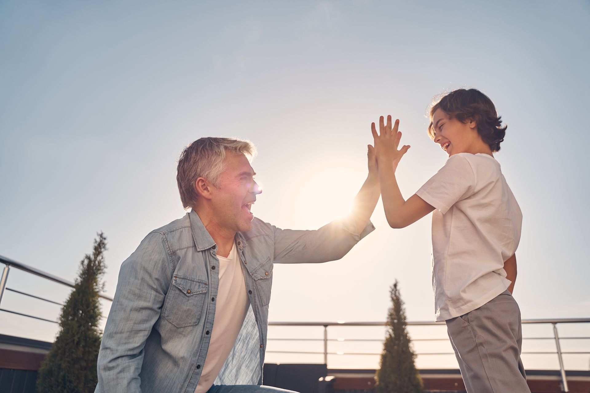 Two people high-five outdoors at sunset, smiling near a rooftop railing.