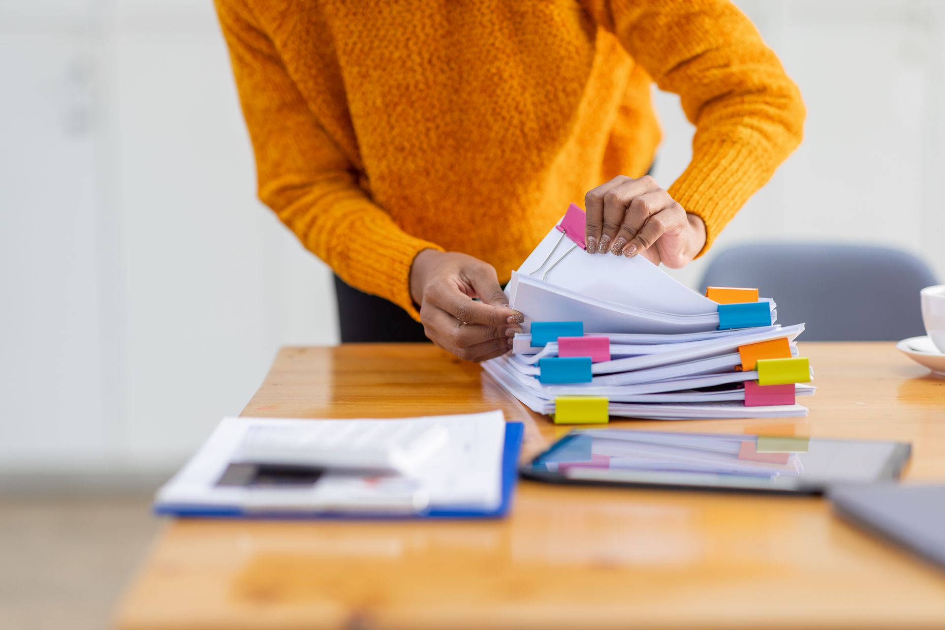 Person in an orange sweater sorting a stack of colorful papers on a desk