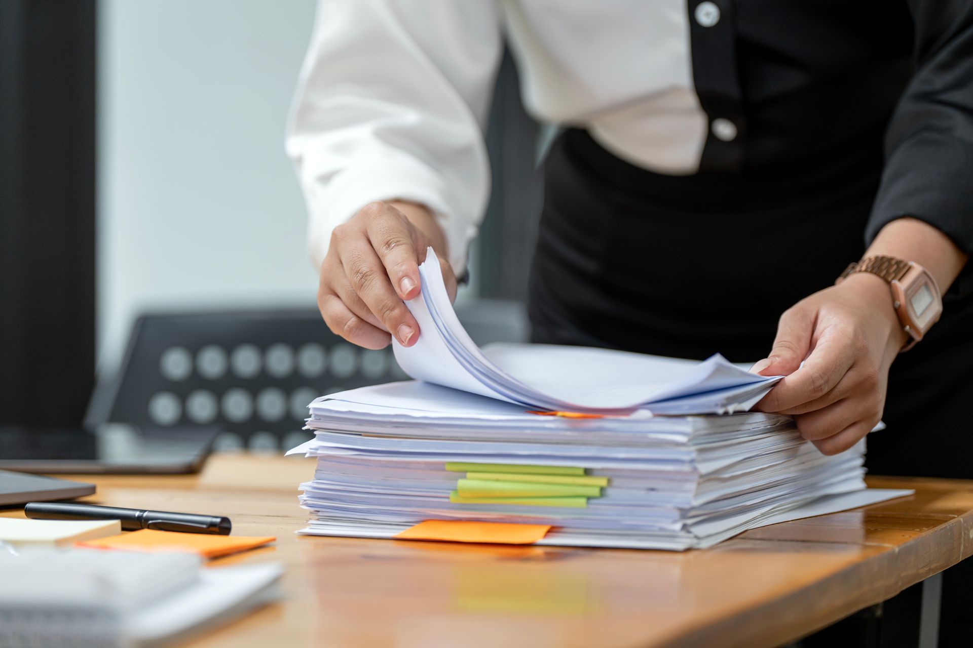 Person sorting a stack of documents on a desk with colored tabs and sticky notes