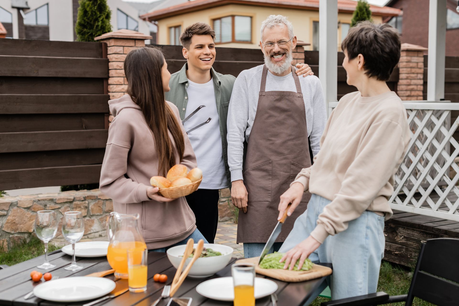Friends chatting around a backyard barbecue with drinks and grilled food outdoors.
